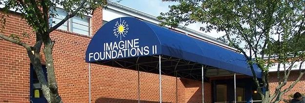 Blue awning reading “IMAGINE FOUNDATIONS II” over a brick building entrance