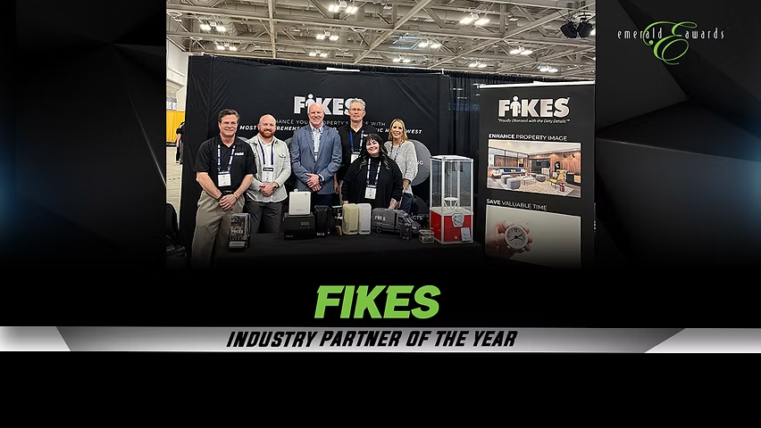 Group posing at a FIKES trade show booth with Industry Partner of the Year banner and product displays.