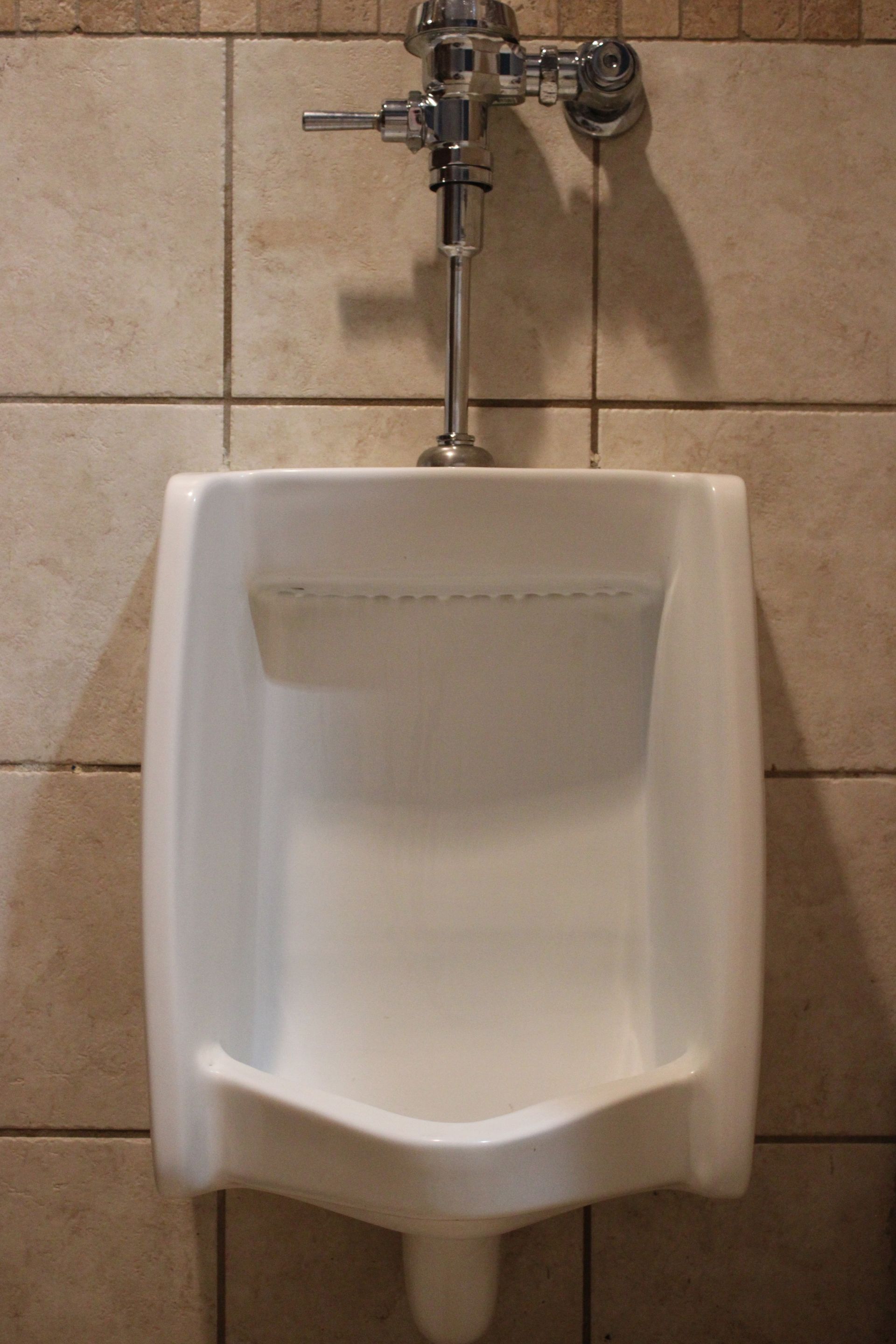 A white wall-mounted urinal in a tiled restroom.