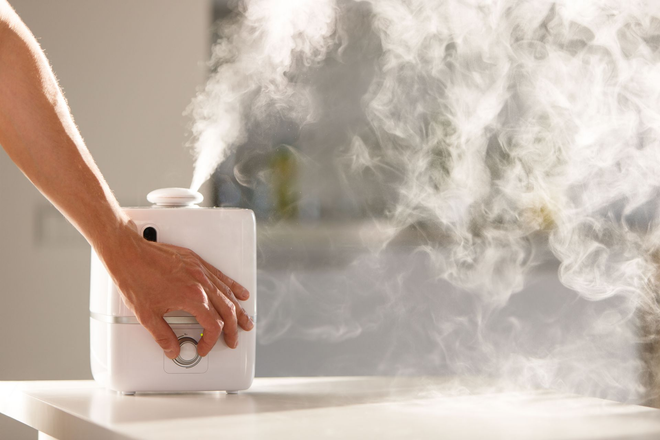 Hand holding a white essential oil diffuser releasing thick mist on a table