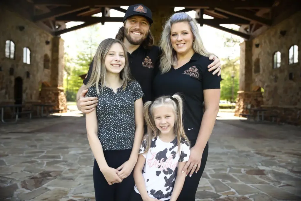 A family of four stands smiling together under a stone archway.