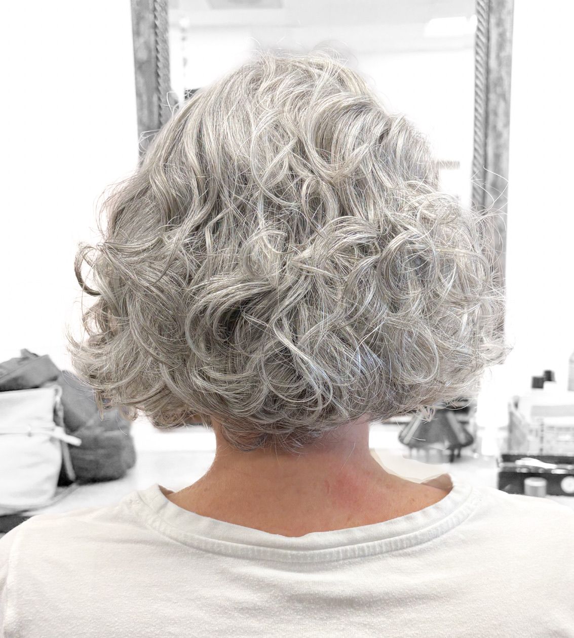 A woman with gray hair is sitting in front of a mirror.
