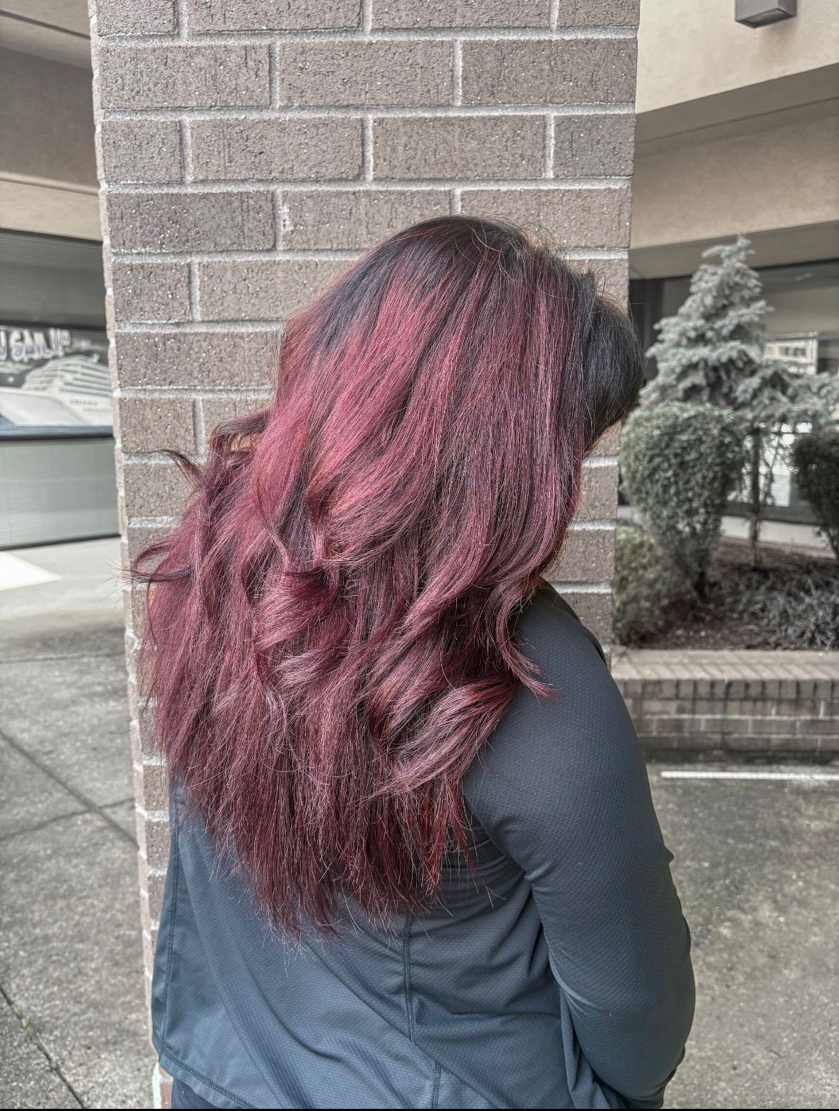 A woman with long red hair is standing in front of a brick wall.