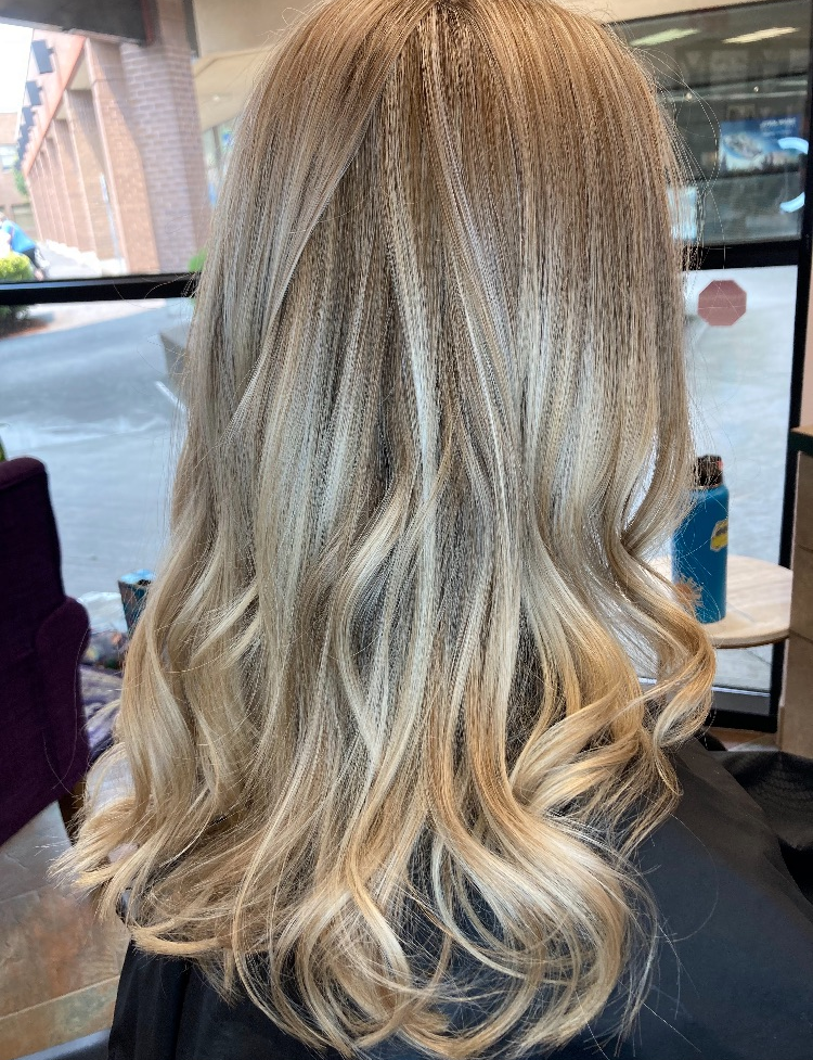 A woman with long blonde hair is sitting in a chair in a salon.