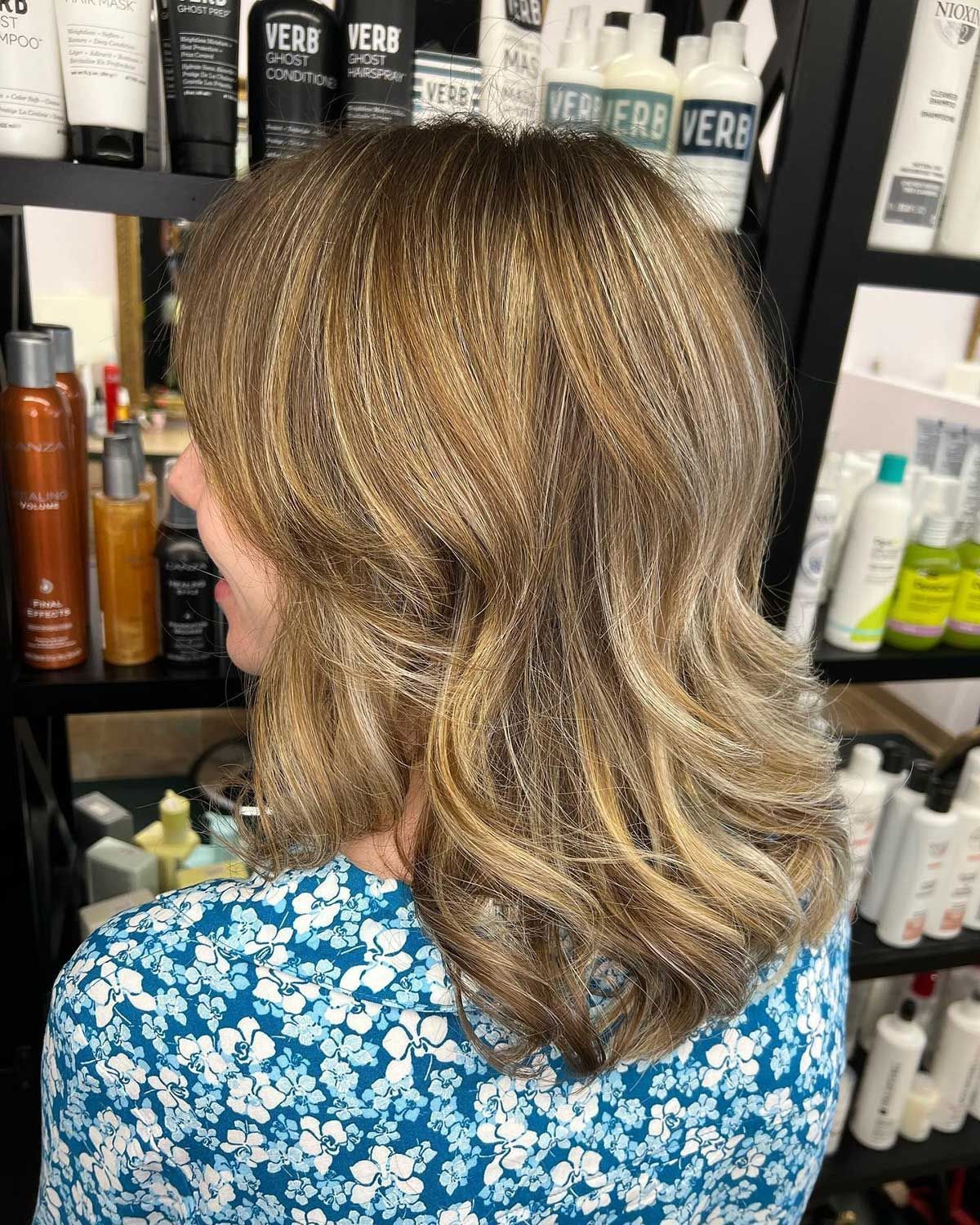 A woman with blonde hair is sitting in front of a shelf of hair products.