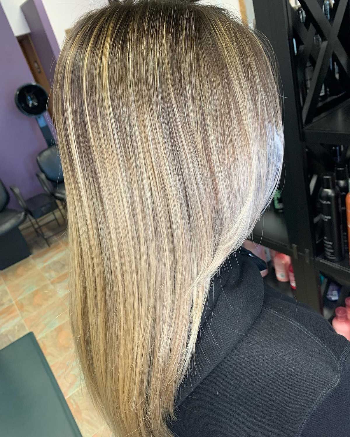 A woman with long blonde hair is sitting in a chair in a salon.