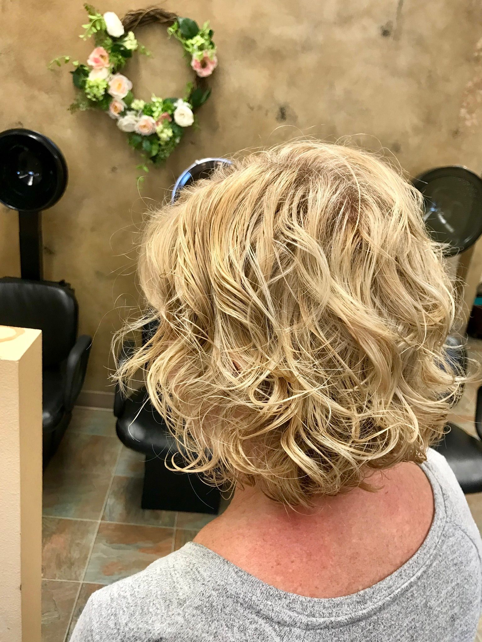 A woman with blonde curly hair is sitting in a chair in a salon.