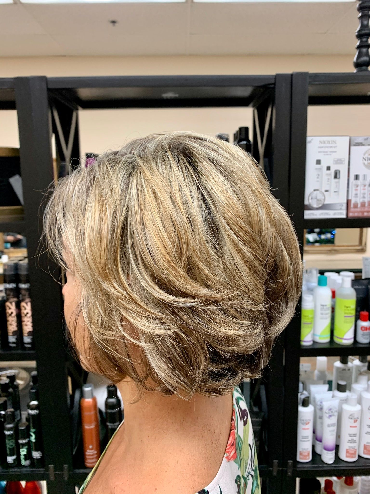 A woman with short blonde hair is standing in front of a shelf filled with hair products.