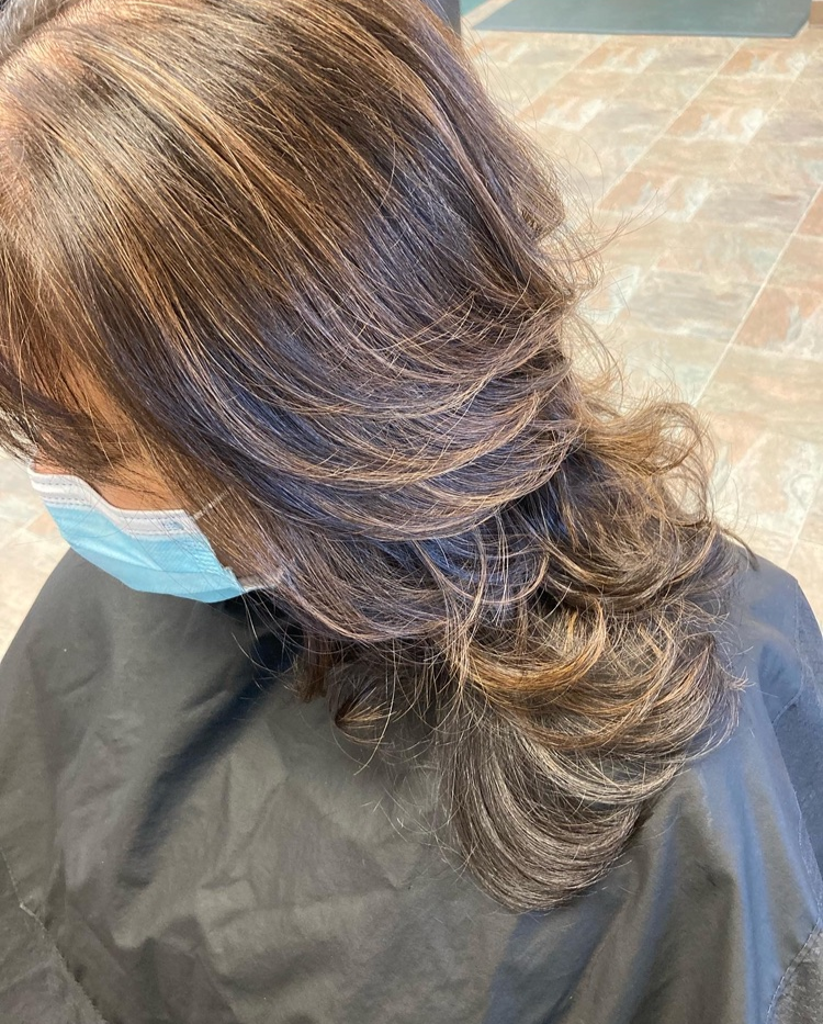 A woman wearing a mask and a cape is getting her hair cut.