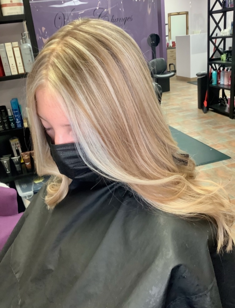 A woman with blonde hair is wearing a black mask in a salon.