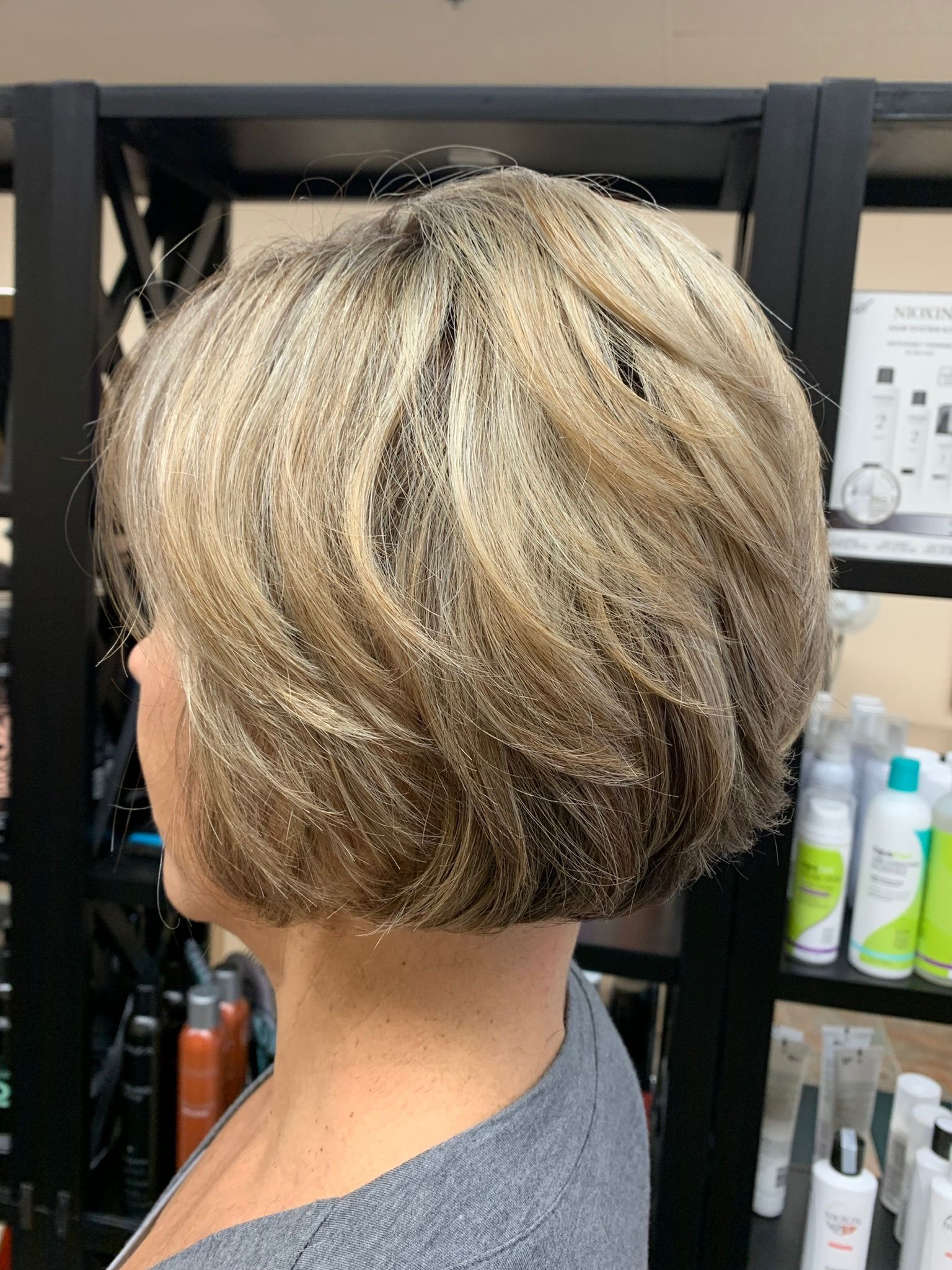 A woman with short blonde hair is standing in front of a shelf of hair products.