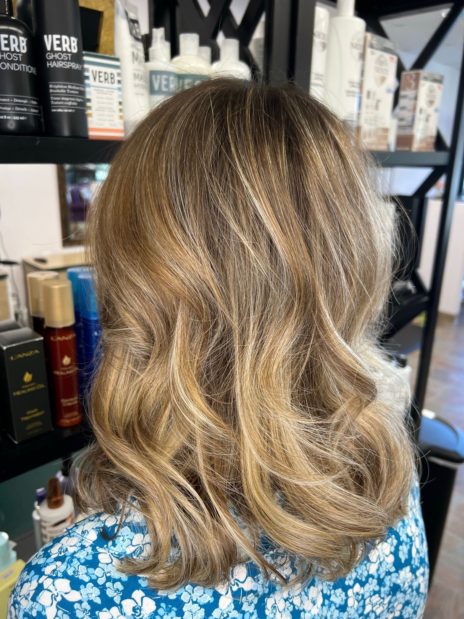 A woman with blonde hair is sitting in a chair in front of a shelf of hair products.