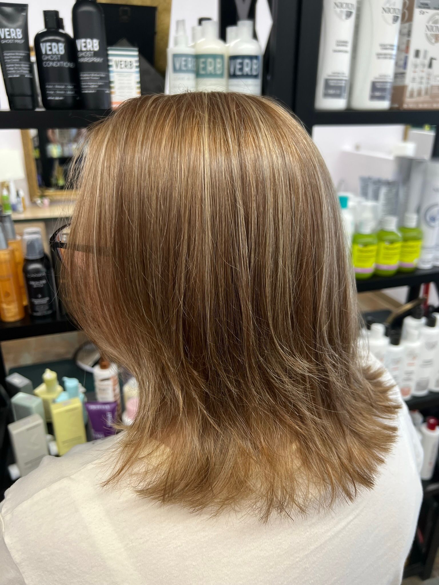 A woman with blonde hair is sitting in front of a shelf of hair products.
