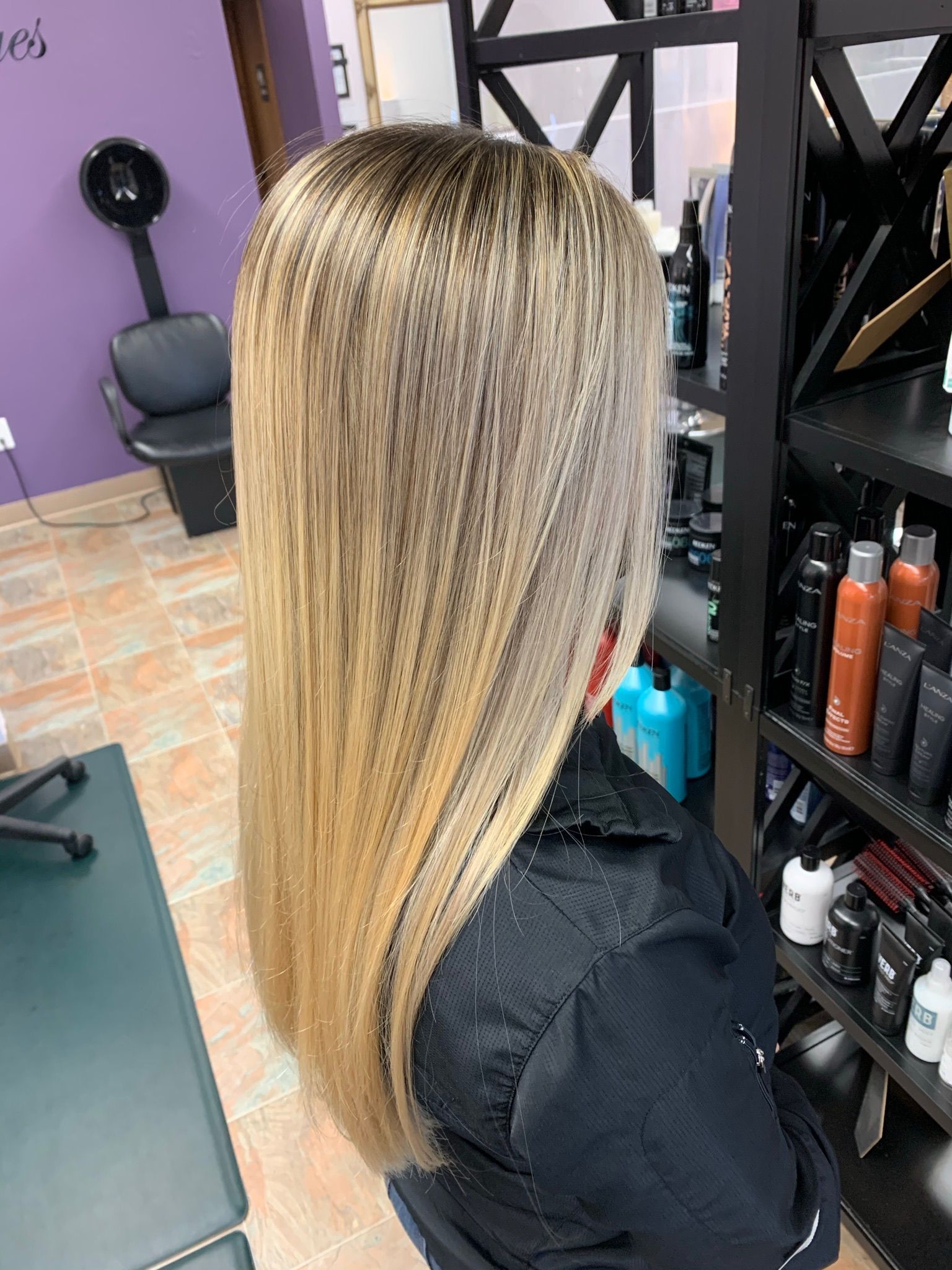 A woman with long blonde hair is sitting in a chair in a salon.