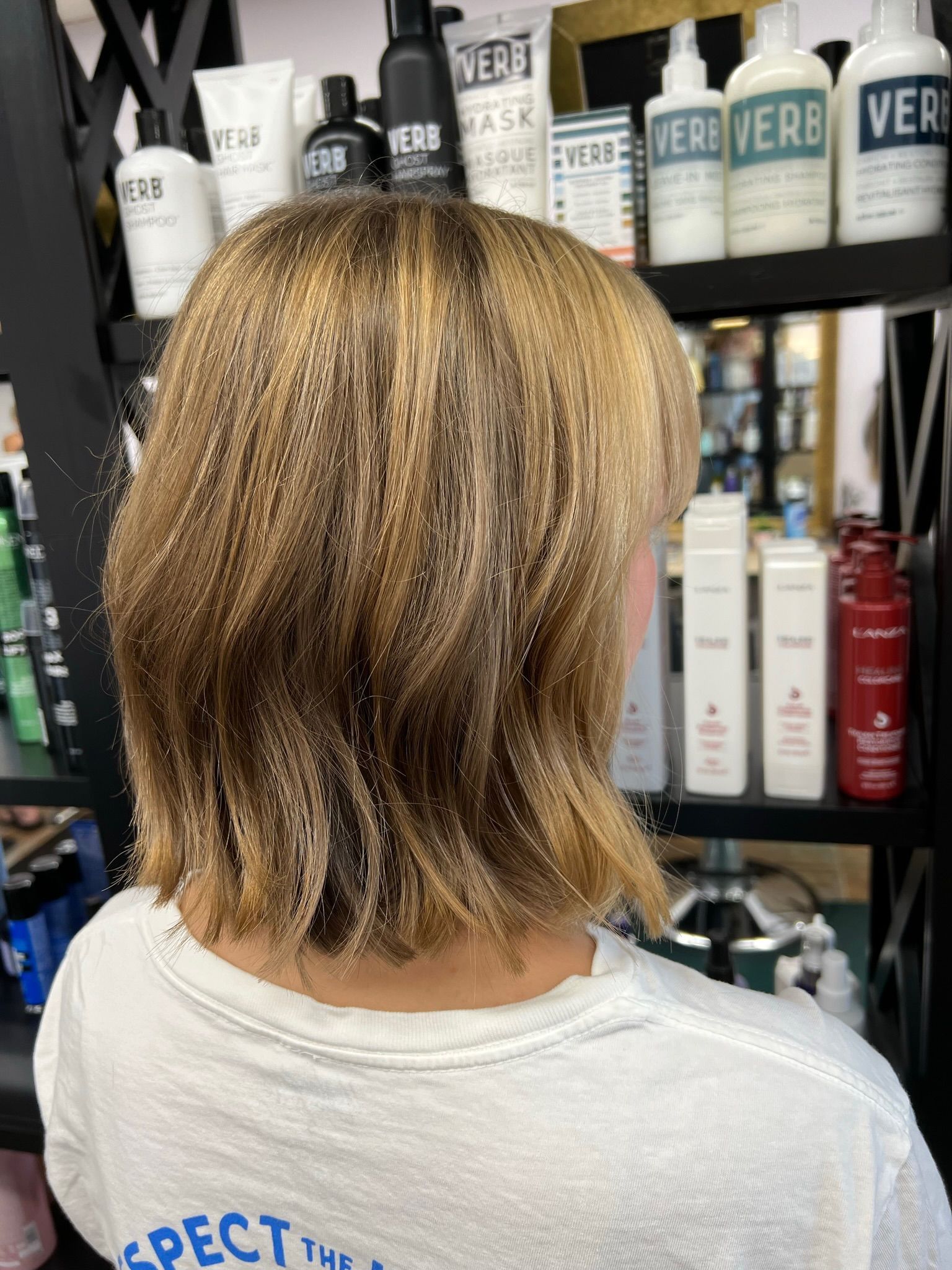 A woman is sitting in front of a shelf of hair products.