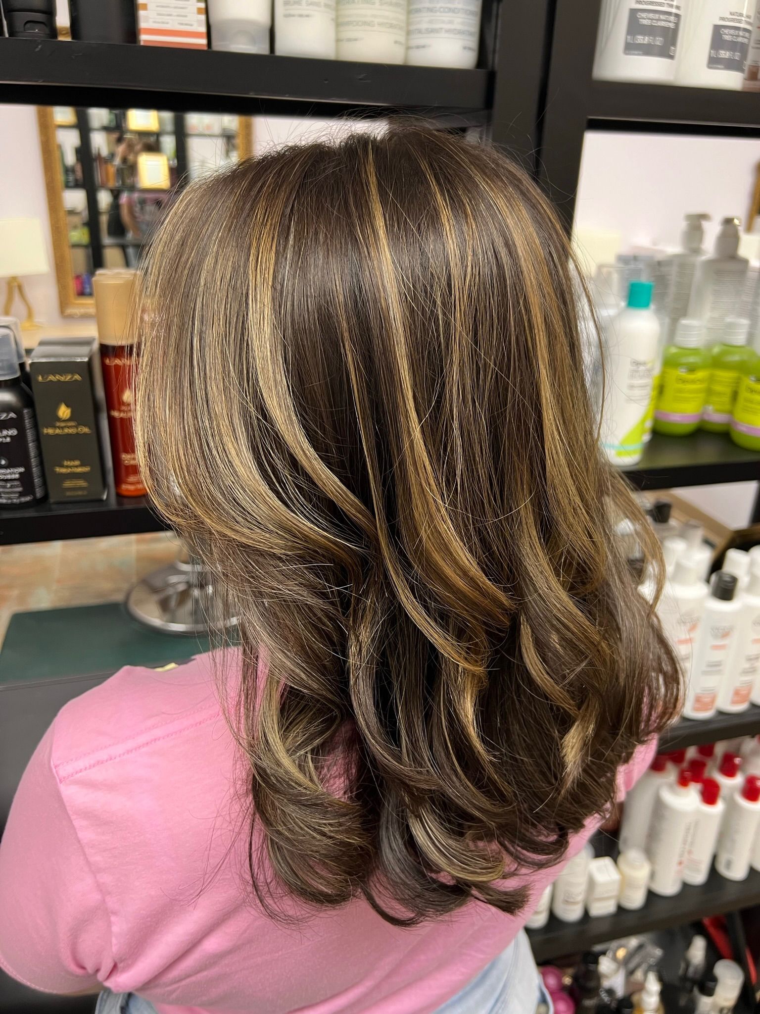 A woman in a pink shirt is standing in front of a shelf of hair products.