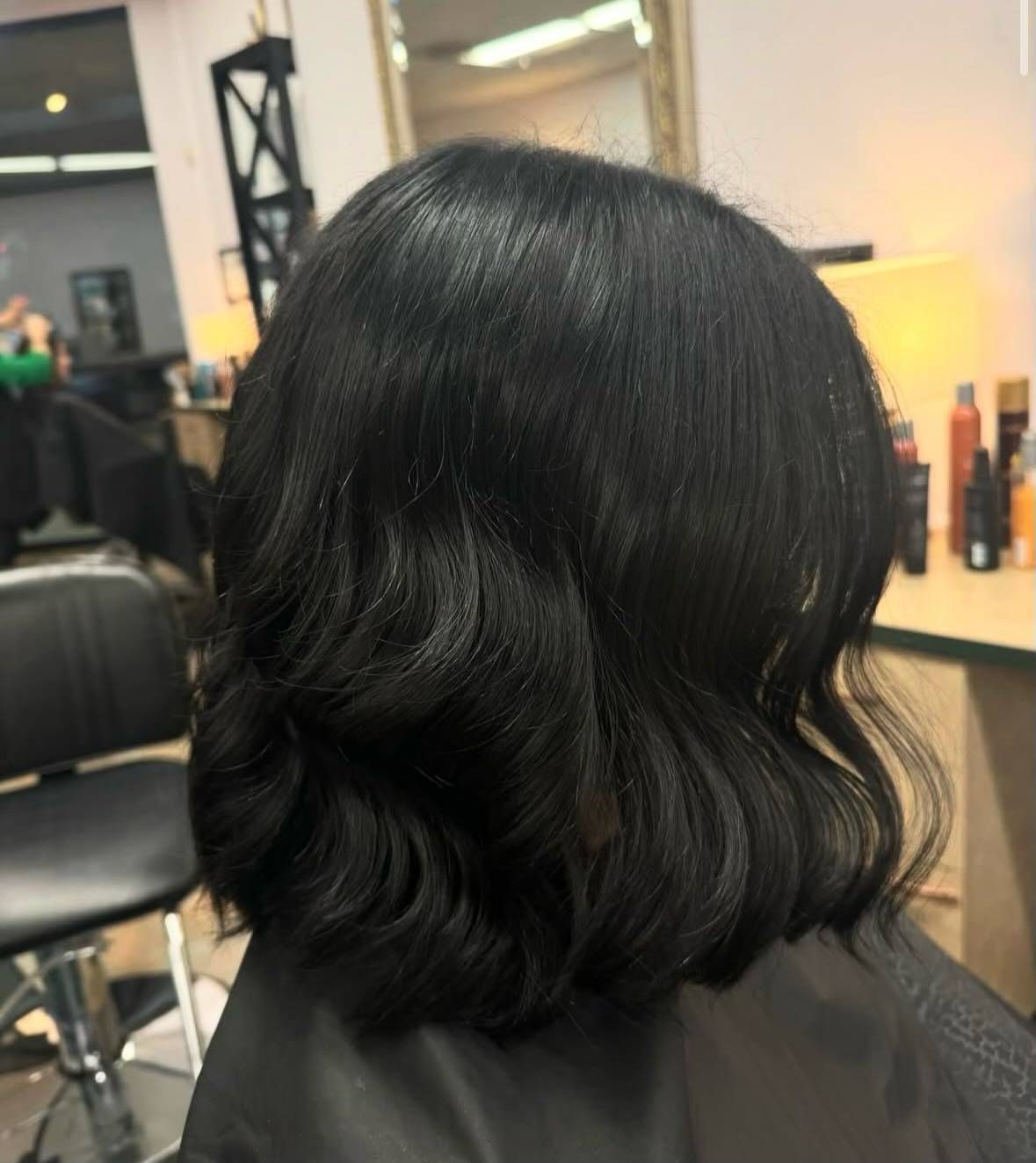 A woman with black hair is sitting in a chair in a salon.