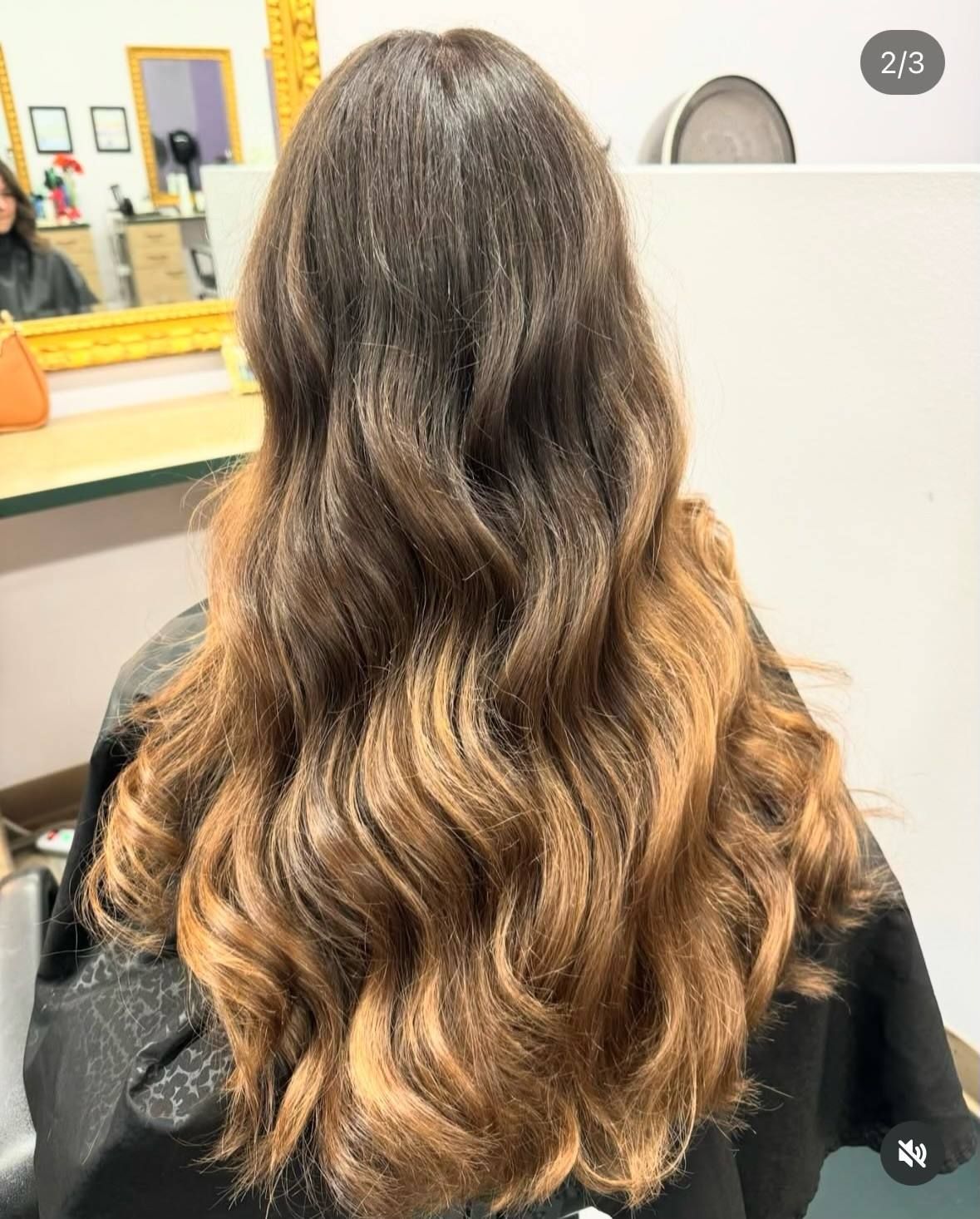 A woman with long wavy hair is sitting in a chair in front of a mirror.