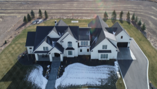 An aerial view of a large white house with black roofs in the middle of a field.