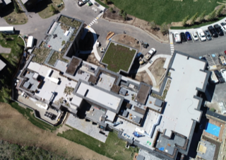 There is a house in the middle of a snowy field with mountains in the background.