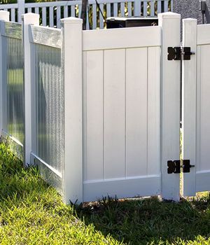A white vinyl fence with a black gate is in the grass.