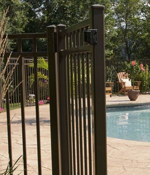 A metal fence surrounds a swimming pool with chairs and flowers in the background.