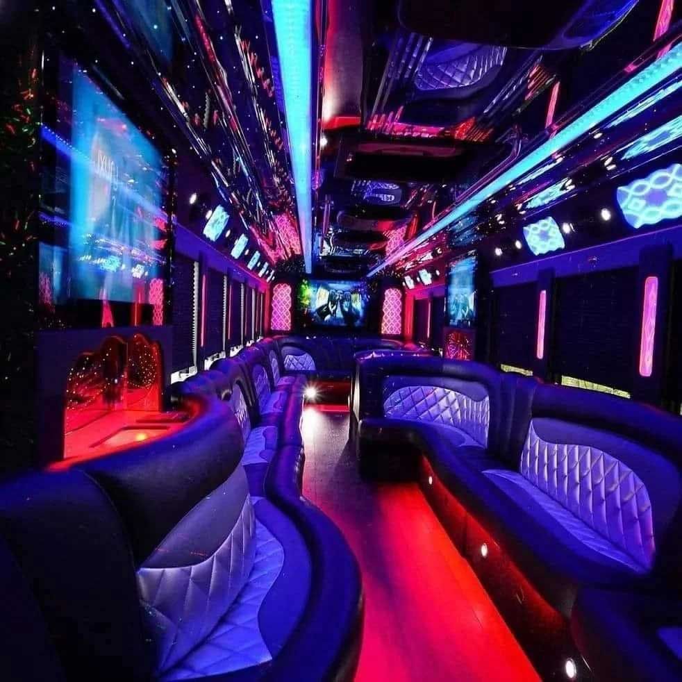 Interior of a party bus with neon blue and red lights, leather seating, and screens.