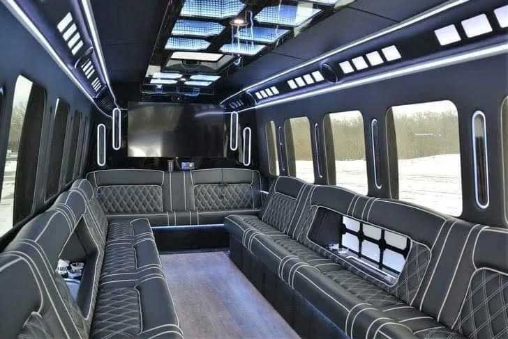 Interior of a luxury party bus with black quilted leather seating, ambient lighting, and large windows.