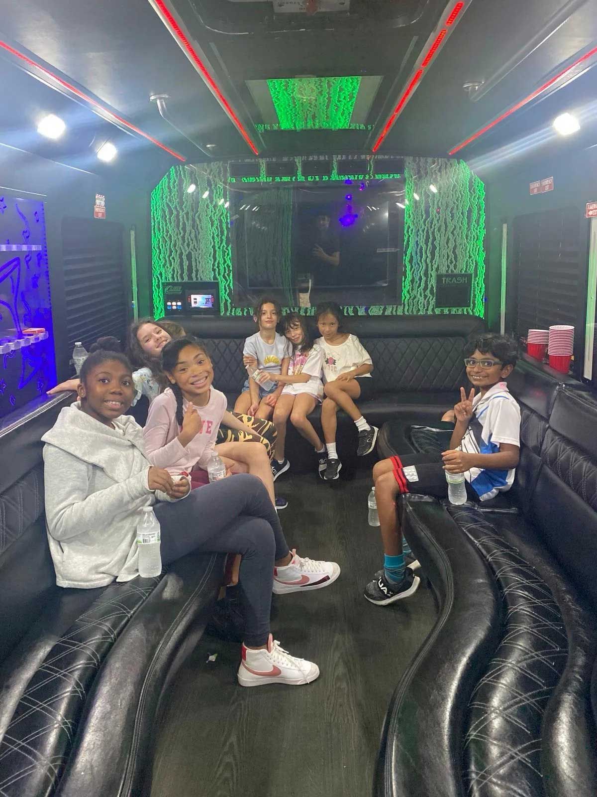 Children sitting inside a party bus with neon lights.