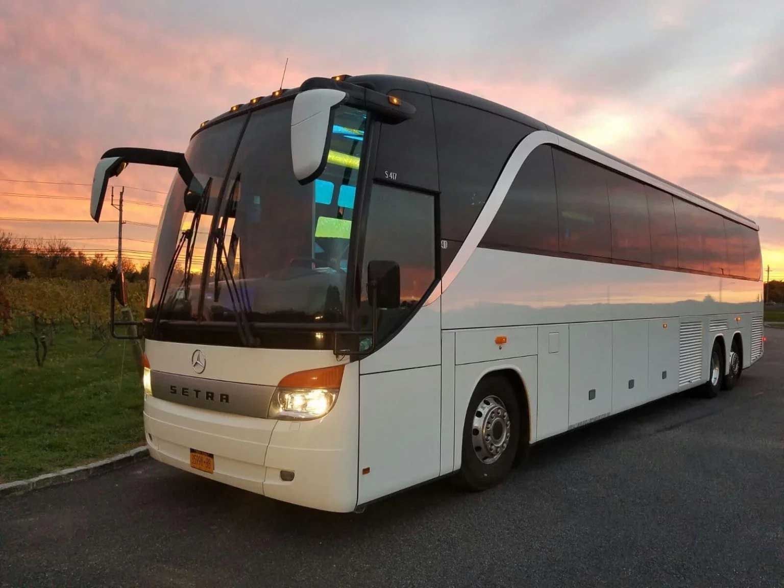 White tour bus parked, sunset sky in background.