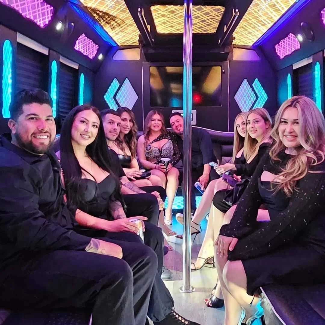 People smiling inside a party bus with neon lights and a stripper pole.