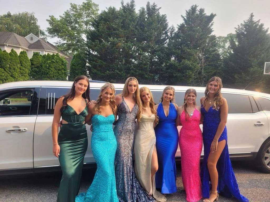 Group of teens in prom dresses posing by a white limousine.