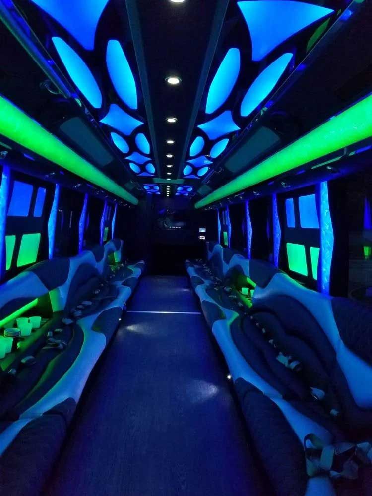 Interior of a party bus with blue and green neon lights illuminating the seats and ceiling.