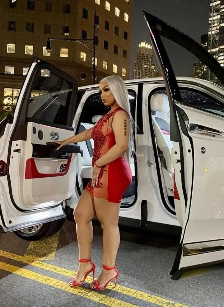 Woman in red dress exiting white car with open doors, city background.
