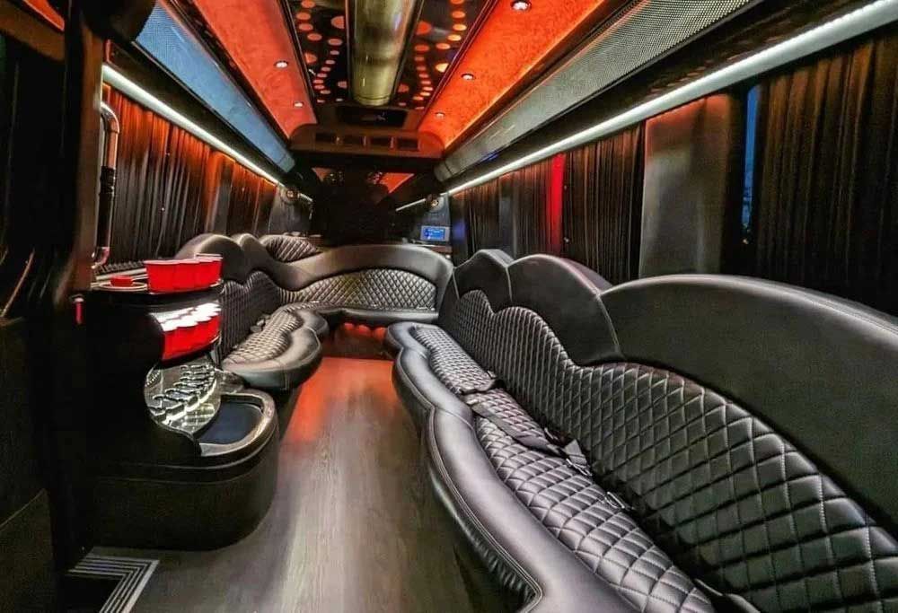 Interior of a luxury party bus with black quilted leather seating and red accent lighting.
