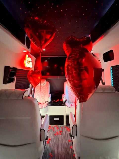 Interior of a vehicle decorated with red heart balloons, lighting, and rose petals for a romantic setting.