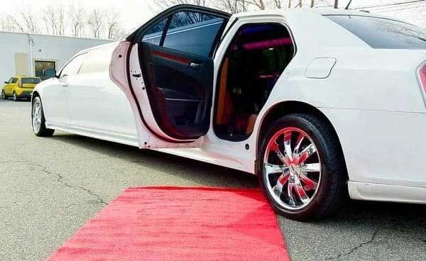 White limousine with open door on red carpet. Chrome wheels.