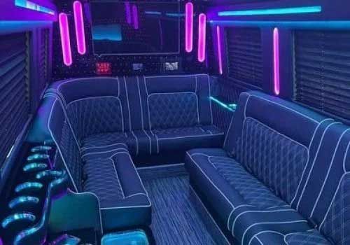 Interior of a party bus with black quilted leather seating and neon purple and blue lighting.
