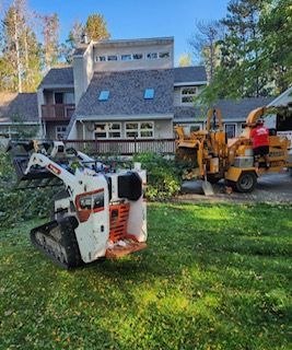 A tractor is cutting trees in front of a house.