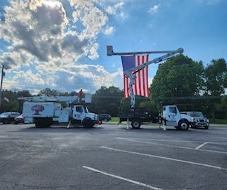 Two trucks are parked in a parking lot with an american flag hanging from a pole.