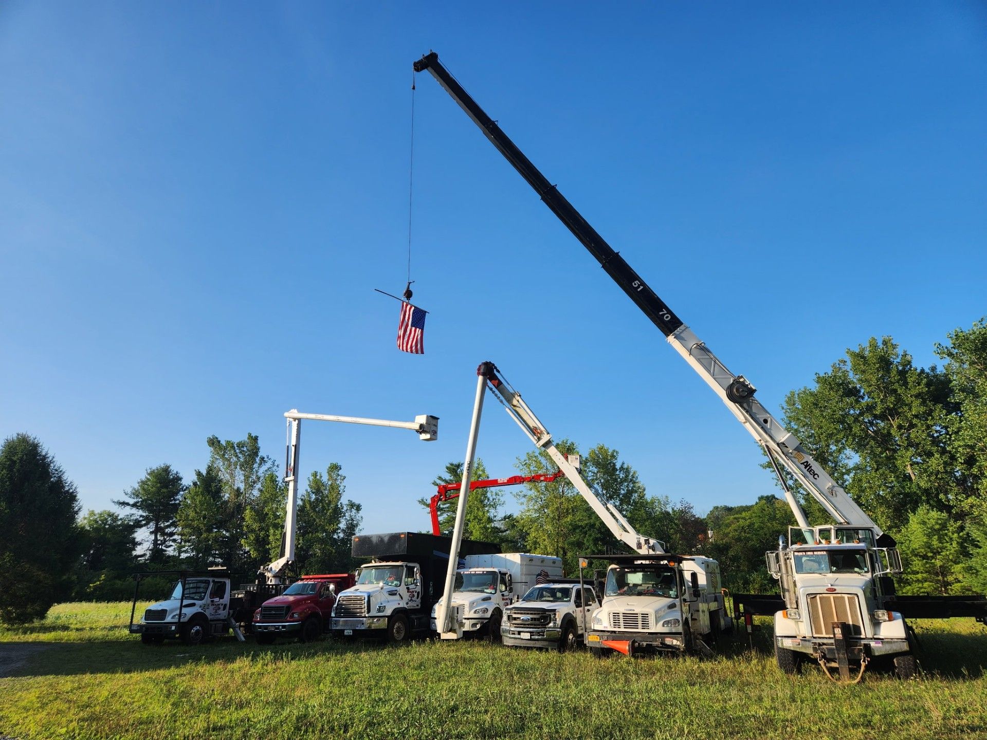 Several utility trucks with raised booms in a grassy field under a blue sky.