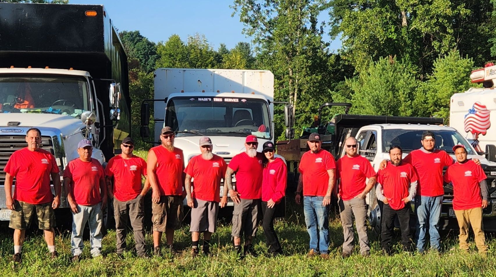 Group of men in red shirts posing with trucks in a grassy field.