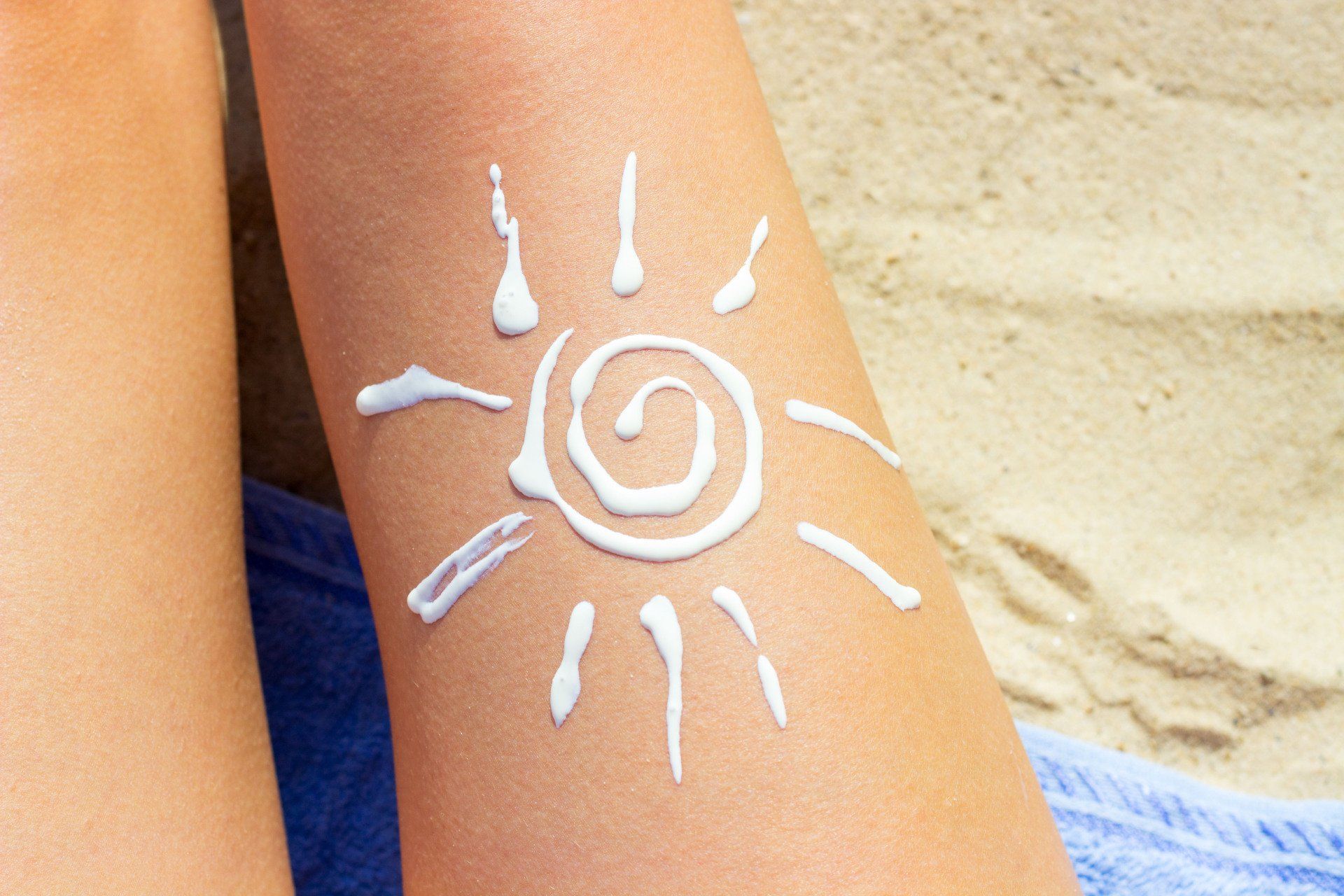 Tan leg with a sun drawn with lotion on it