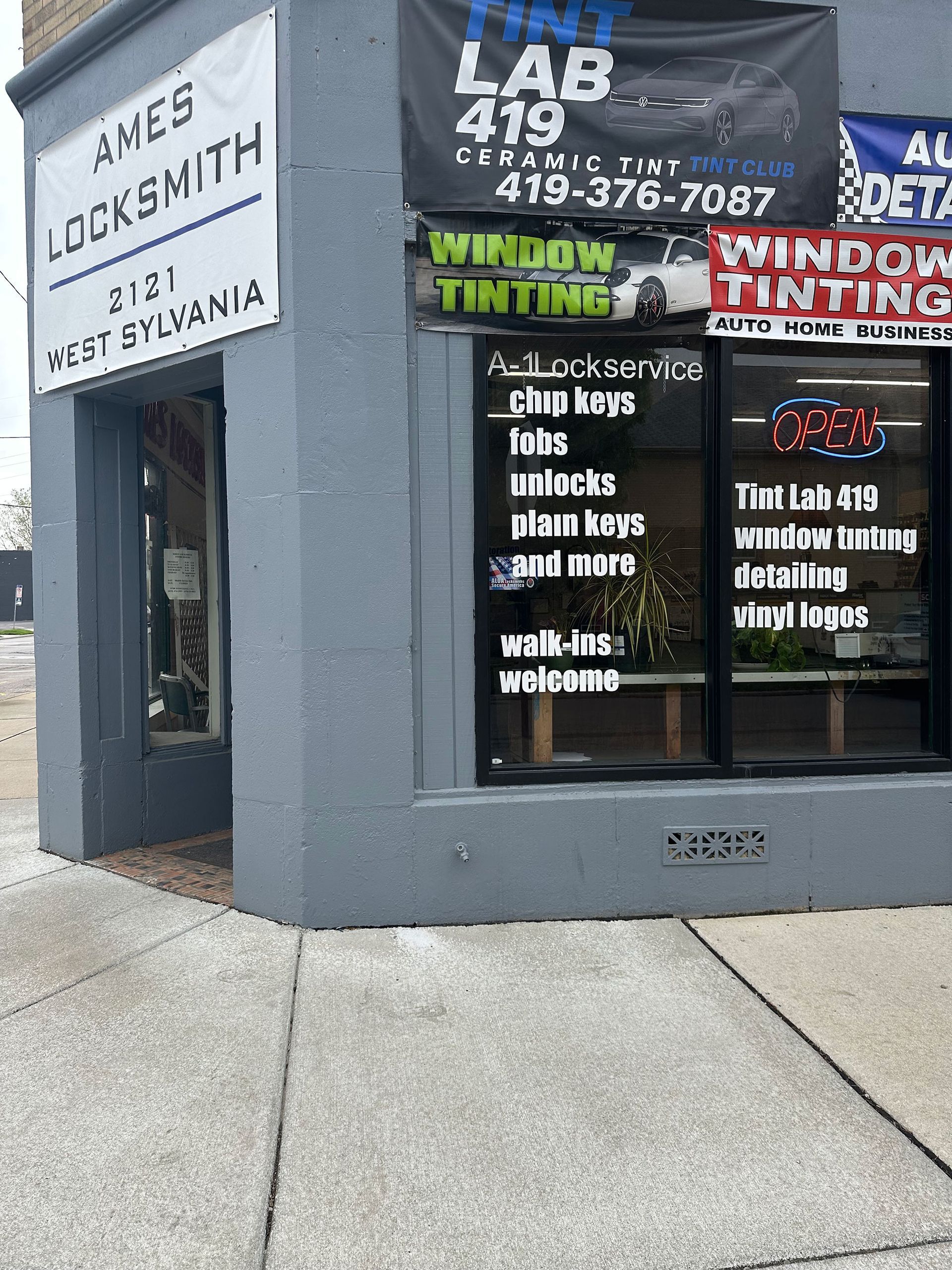 Gray storefront with Shoe and Locksmith signs, plus ads for lab, window tinting, and tattoos