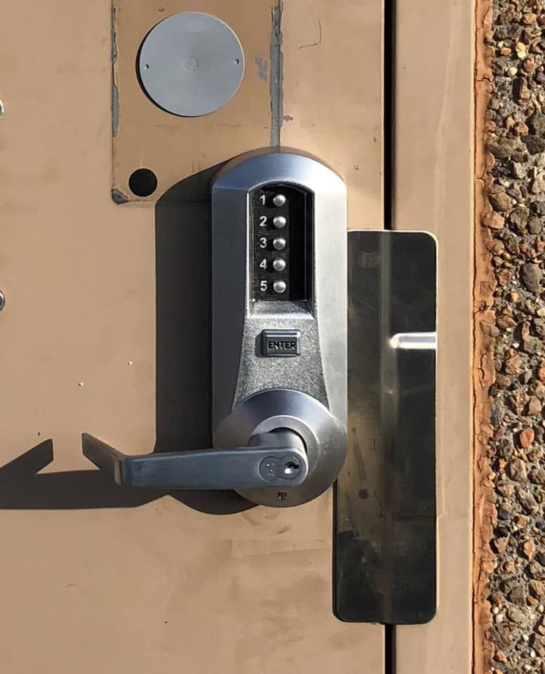 Keypad door lock with lever handle on a tan metal door, shown close up.