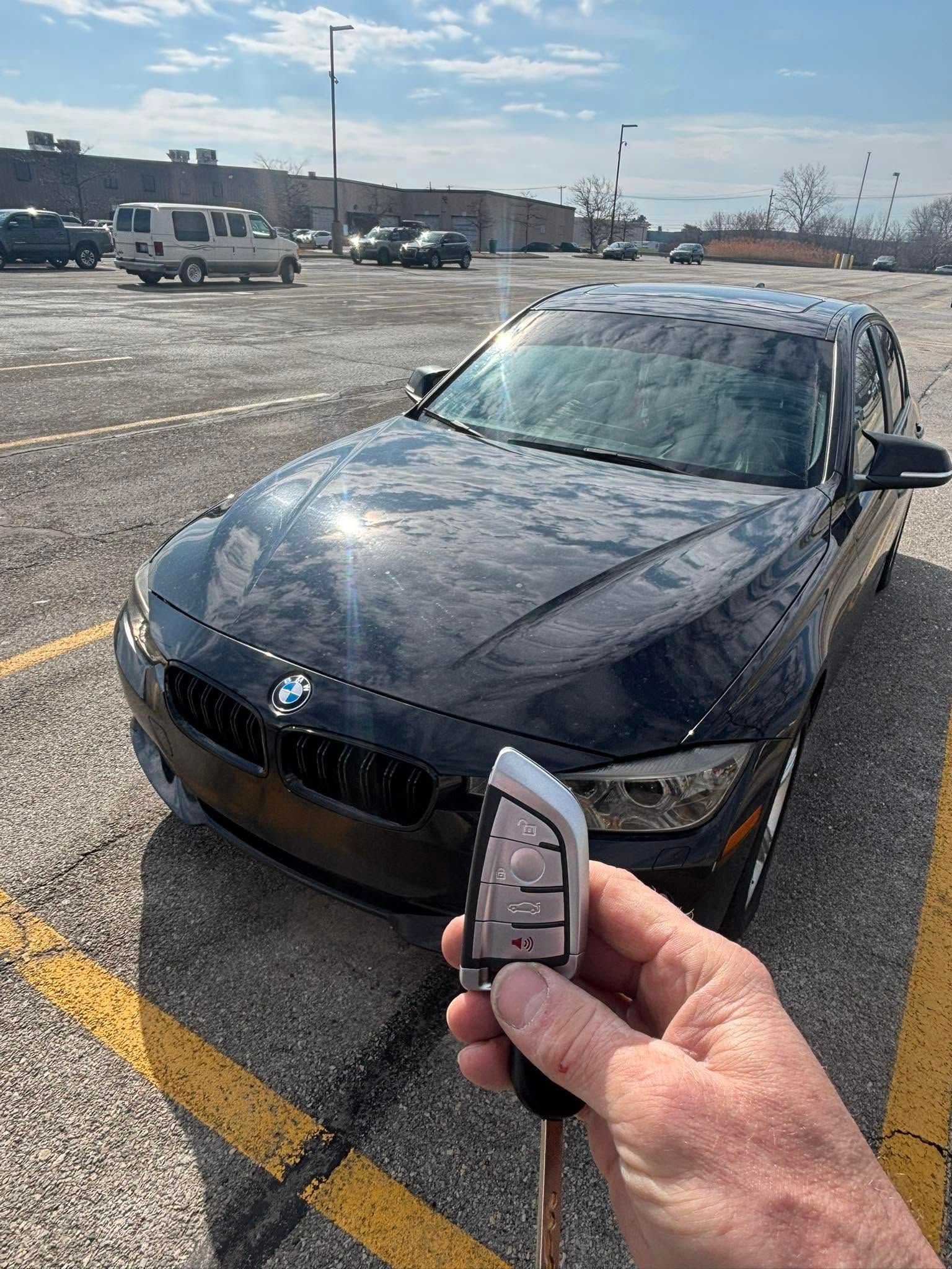 Hand holding a car key fob in front of a black BMW parked in a snowy lot