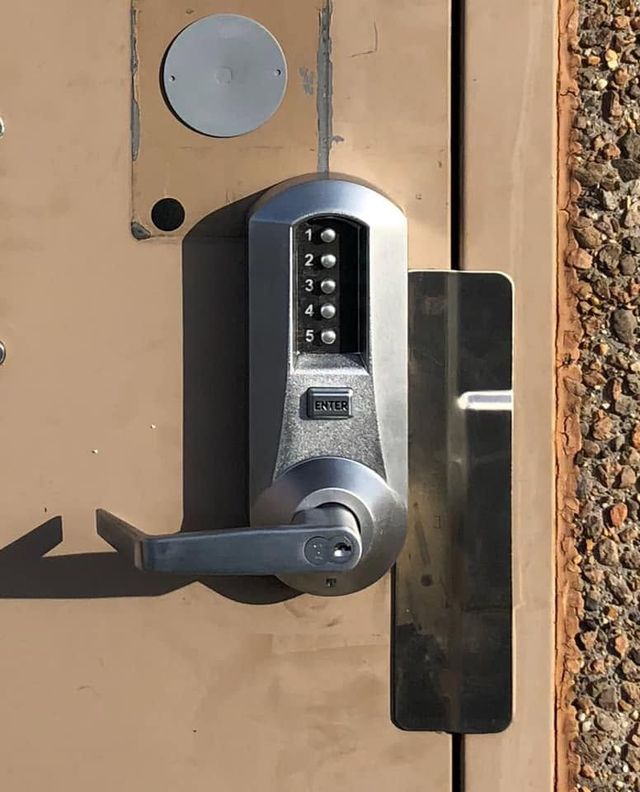 Close-up of a keypad door lock on a tan metal gate with a black handle.