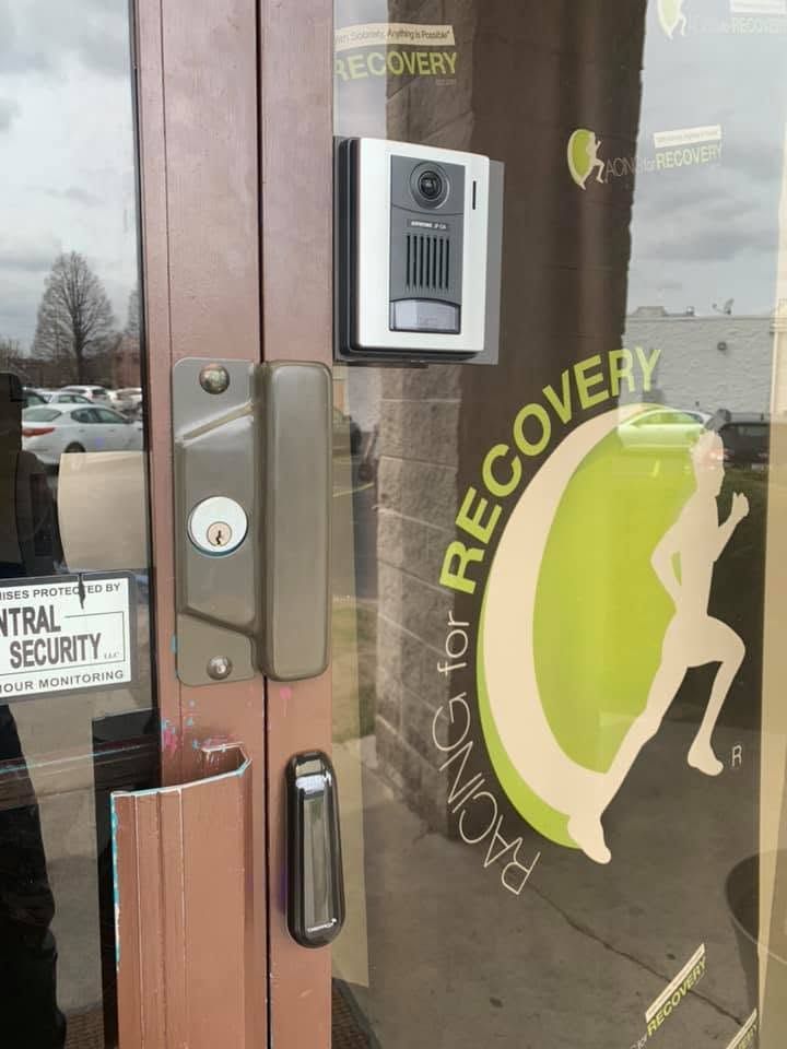 Glass storefront door with metal handle and intercom keypad beside a “Recovery” logo decal.
