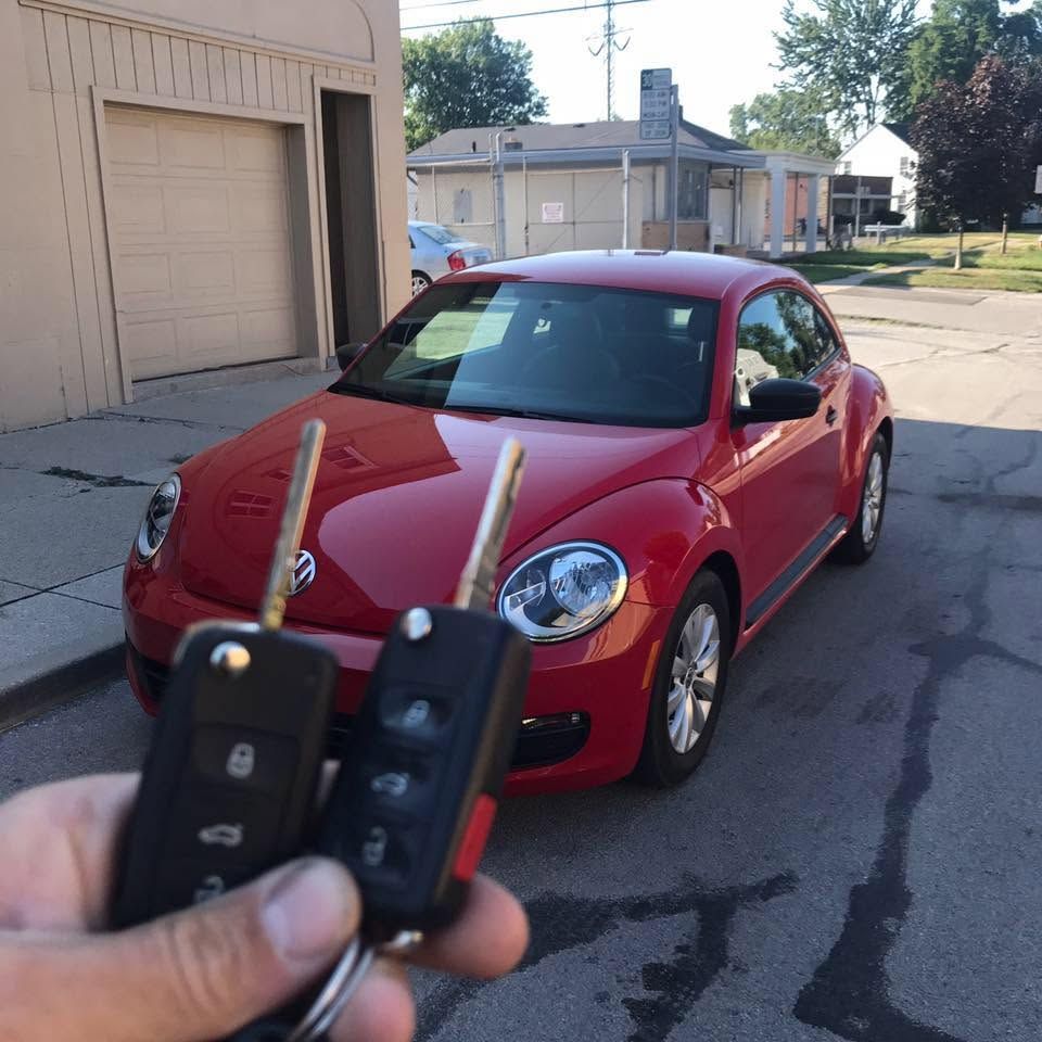 Hand holding two car key fobs in front of a red coupe parked on a street