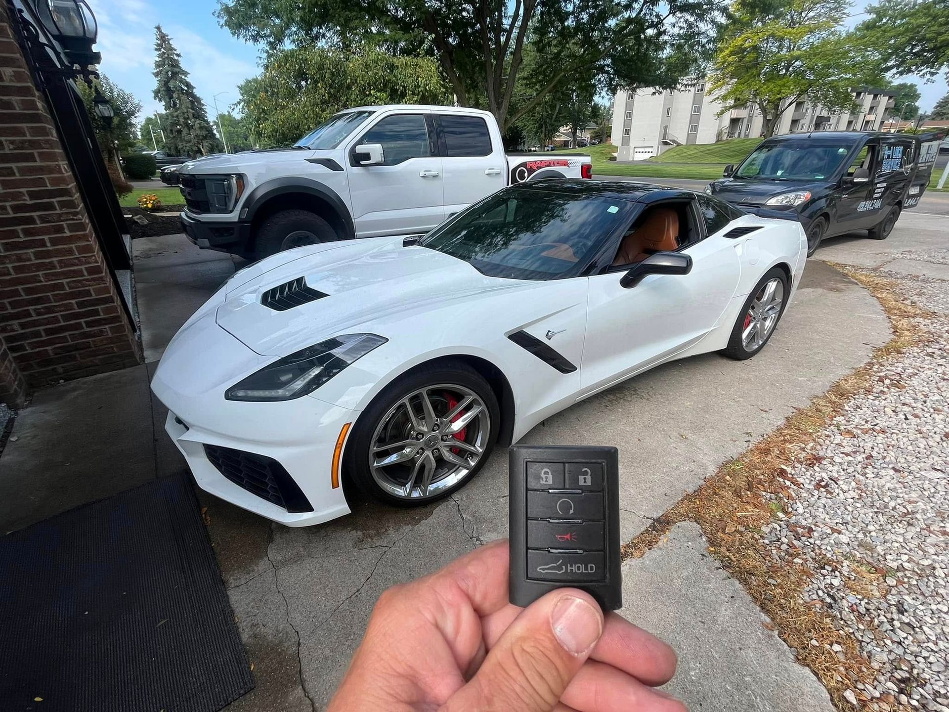 White sports car in a driveway, with a hand holding a key fob in the foreground.